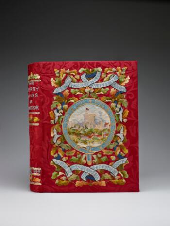 A book with a colourful embroidered cover. The background is a red brocade silk. At the centre of the cover a round view of Windsor Castle is framed by the blue ribbon of the Order of the Garter, embroidered with its motto 'Honi soit qui mal y sense.' Above and below are further ribbons bearing quotes from the play ('Strew good luck ouphes in every sacred room/ That it may stand till the perpetual doom'), strung across a backdrop of oak leaves and acorns. On the book's spine, the title 'The Merry Wives of Windsor' can be seen embroidered in blue thread, and the date A.D. 1914, with further oak leaf and acorn motifs.